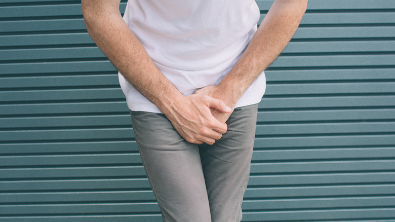 man crossing legs and covering pelvis