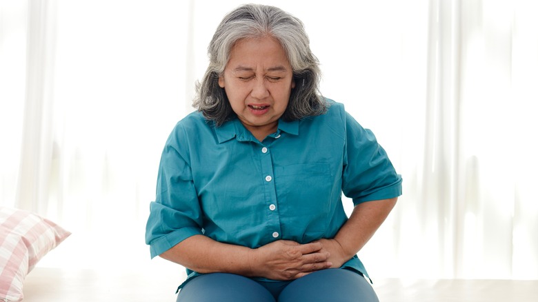 Wincing older woman holding stomach