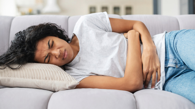 Woman lying on couch holding stomach in pain