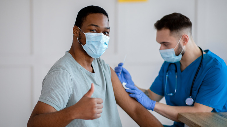 man making thumbs up sign while getting vaccination