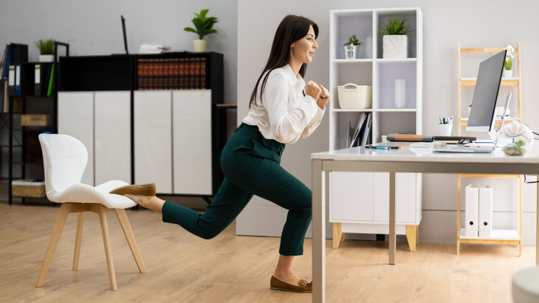 A woman doing a Bulgarian split squat at her office