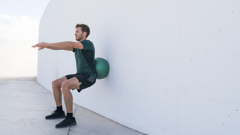 man doing squats against ball