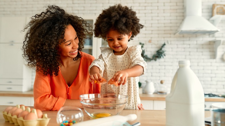 Mother and daughter cracking eggs in kitchen