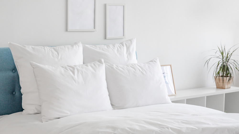 White pillows, duvet and duvet case on bed. White bed linen on a blue sofa. Bedroom with bed and bedding and poster frame mock up on the wall. 