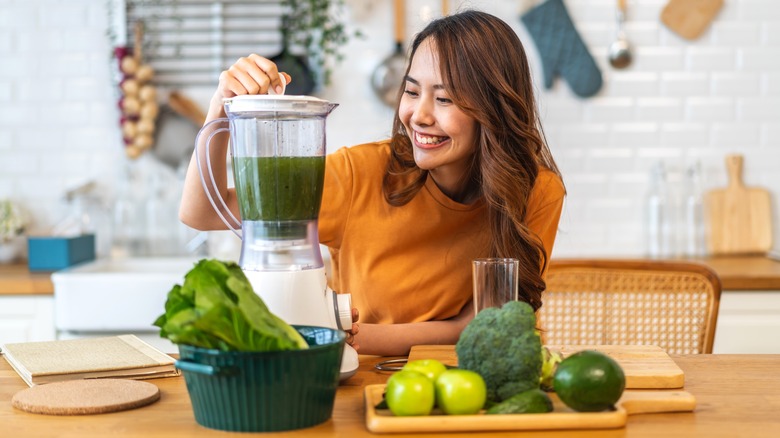 woman adding healthy vegetables to her blender