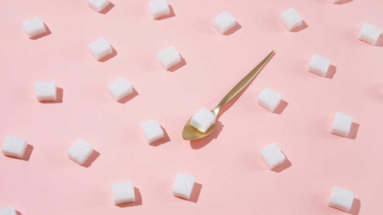 sugar cubes on pink background and golden spoon