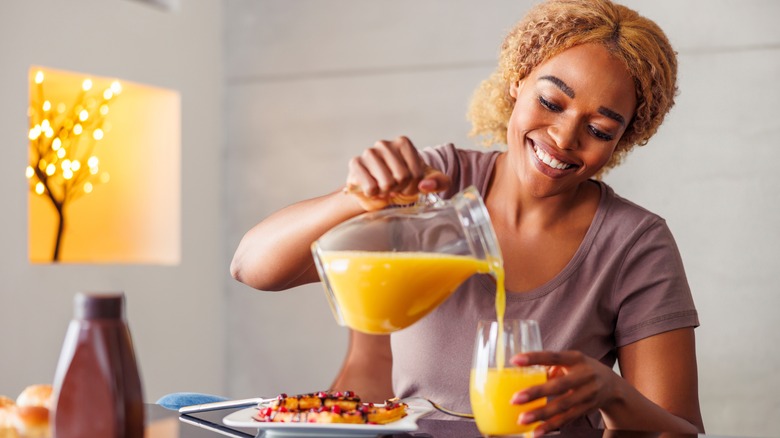 Smiling woman pouring glass of orange juice