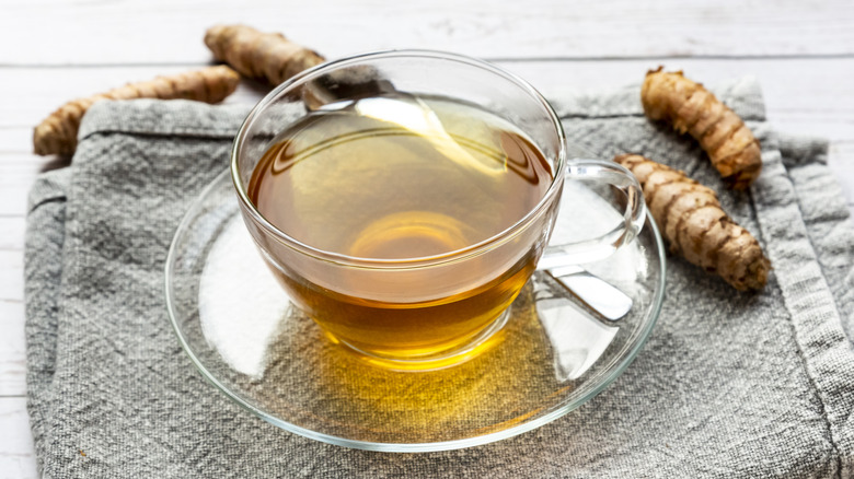 Une tasse en verre de thé au curcuma avec racine de curcuma