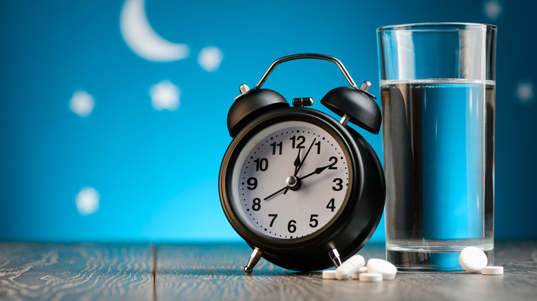 water, alarm clock, and pills on a table