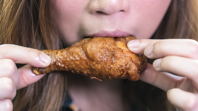 Girl taking a bite out of a chicken drum