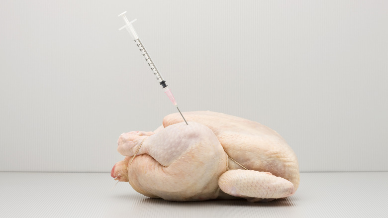 Whole raw chicken with a needle representing antibiotic use