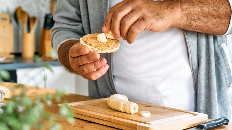 man's hand adding banana slices to peanut butter rice cake