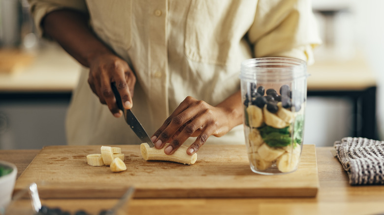 woman's hand cutting a banana for a smoothie