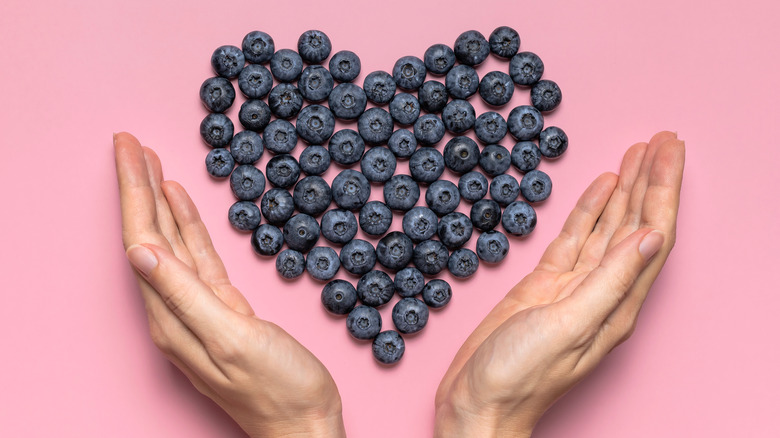 hands with heart-shaped blueberry arrangement