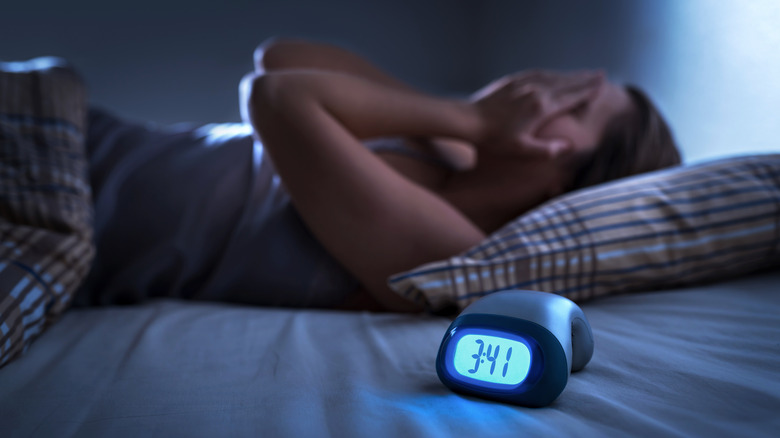 Woman lying restlessly in bed next to a clock reading "3:41"