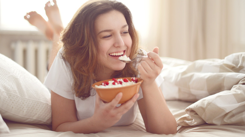 young woman on bed eating cottage cheese