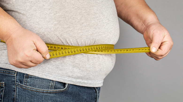 overweight man measuring waistline