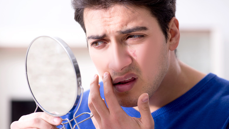 man with mirror looking for pimples