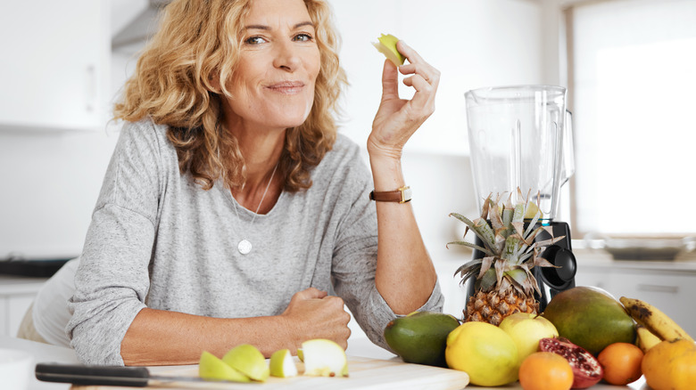 Happy woman eating fruits in kitchen