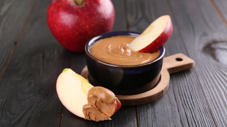 ramekin of peanut butter surrounded by apple slices