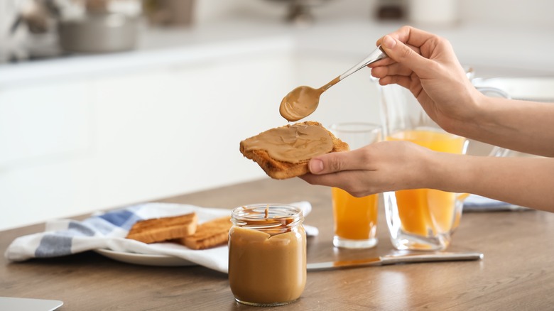 woman's hand spreading peanut butter on toast
