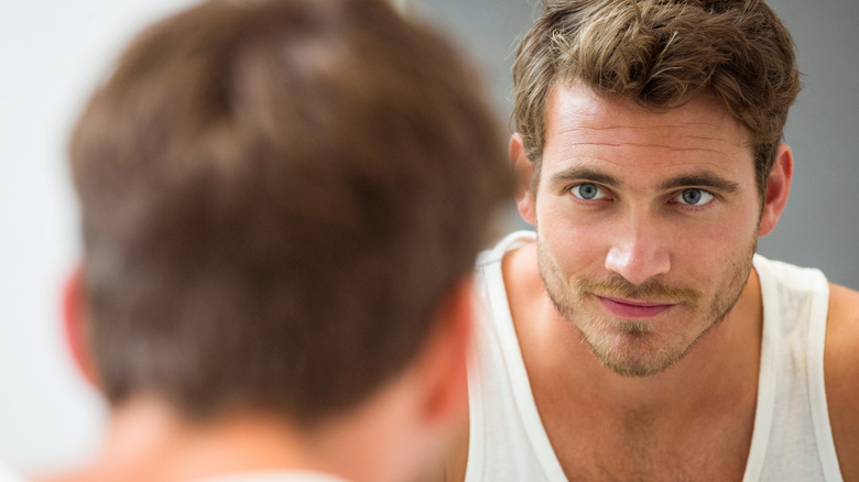 satisfied man looking at himself in bathroom mirror