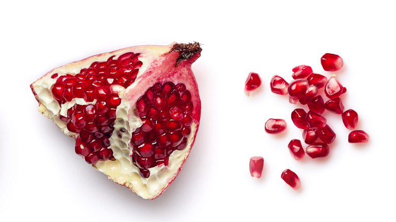 half of a pomegranate next to pile of seeds