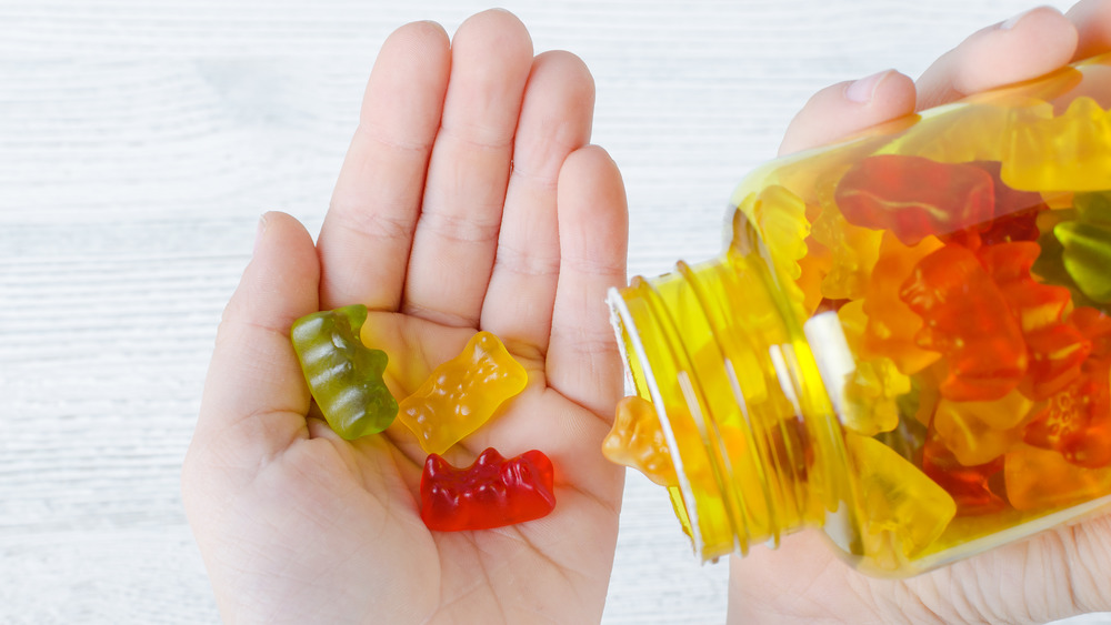 Vitamin gummies in a child's hand, next to jar