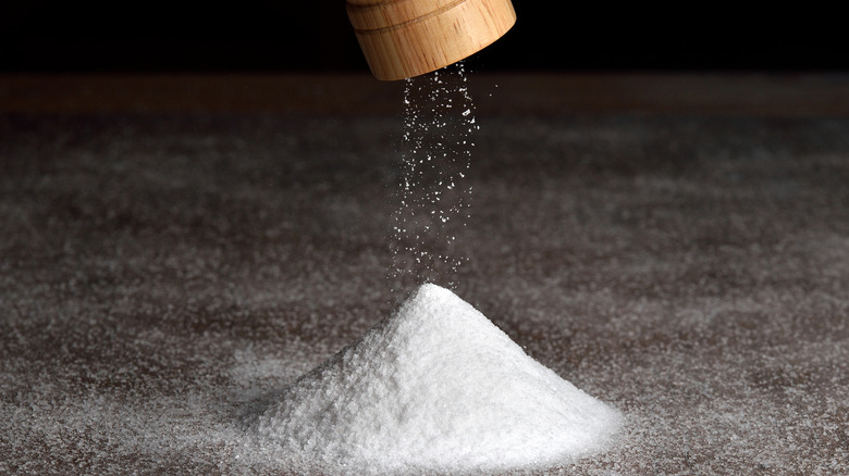 A salt grinder piling salt on a countertop against a dark background