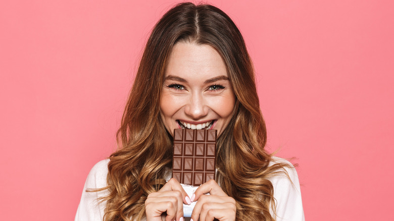 woman biting into a chocolate bar smiling and happy