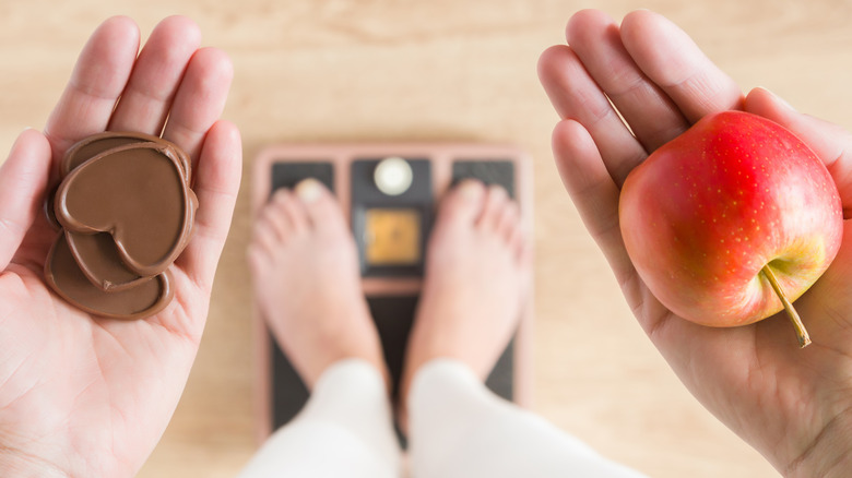 Woman trying to decide between an apple and chocolate