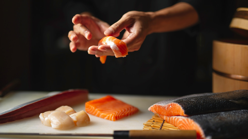 Close up of hands preparing a salmon sushi roll against a black background