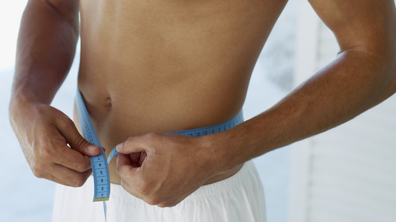Man assessing weight loss with tape measure