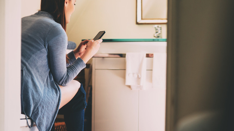 Woman sitting on toilet using smartphone