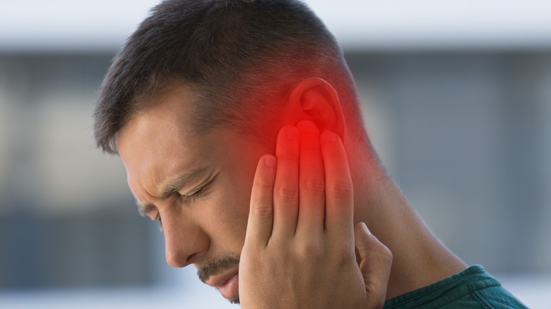 a man holds his ear with pained look