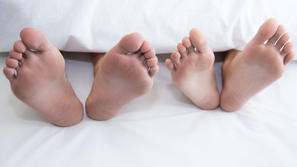 Two pairs of feet in a bed, next to each other