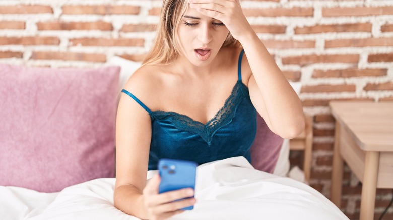 woman in bed surprised reading phone