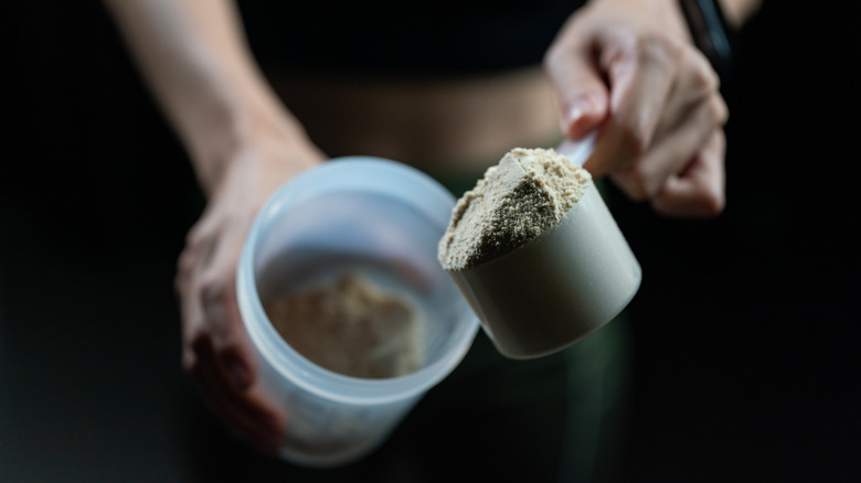 hands pouring protein powder into cup 