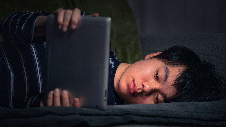 Young boy laying on couch playing on a tablet