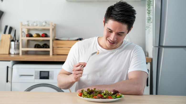 Young smiling man eating salad 