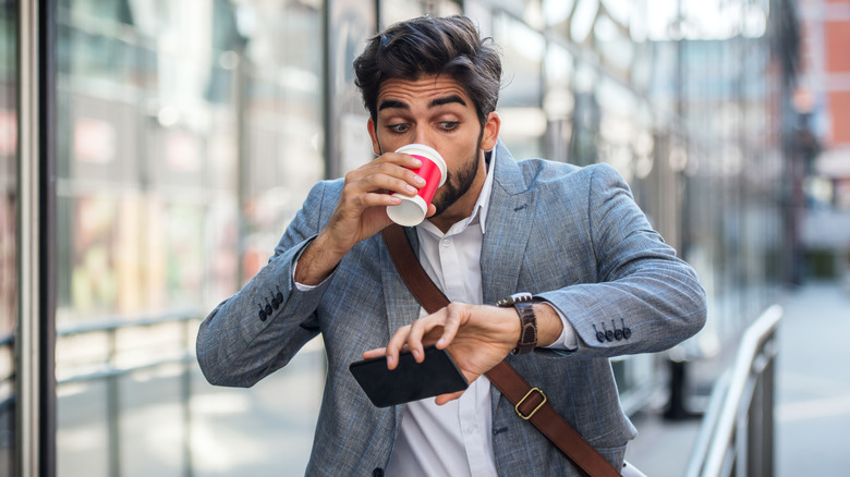 A man drinking coffee while looking at his watch