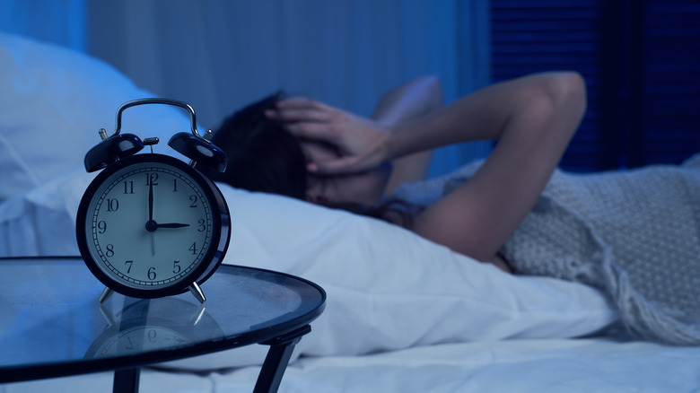 Woman lying awake in bed with clock