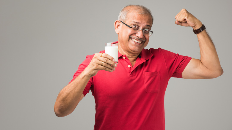 elderly man holds glass of milk and shows off arm muscles