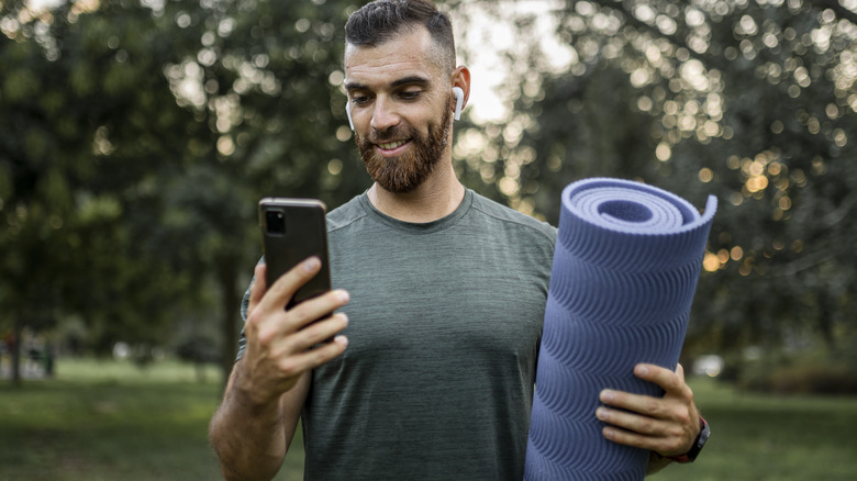 man carrying exercise mat checking phone