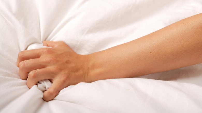 hand grabbing bed sheet in pleasure