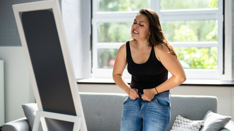 woman struggling to button her jeans