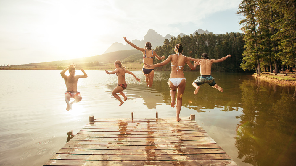 Friends jumping off dock into lake