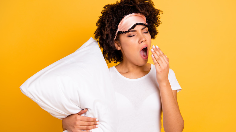 Woman in sleep mask holding a pillow and yawning
