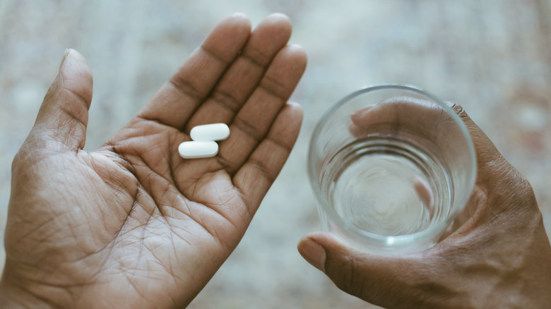 man's hand holding medication and a glass of water