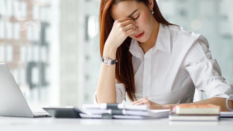 woman rubs eyes at desk